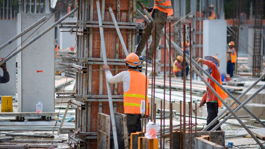 Construction workers in hard hats and high-visibility vests assembling formwork and rebar for concrete columns on a busy building site